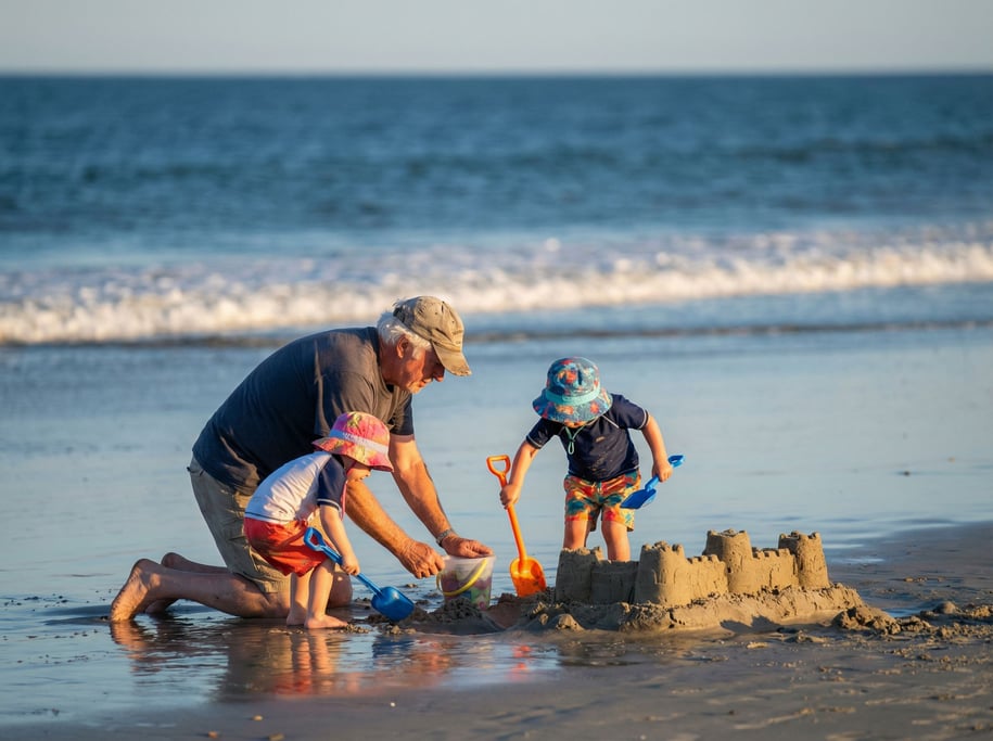 Two kids and their grandfather building a sandcastle on a beach