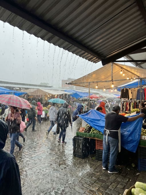 A crowd in a rain-soaked outdoor market scrambling for cover