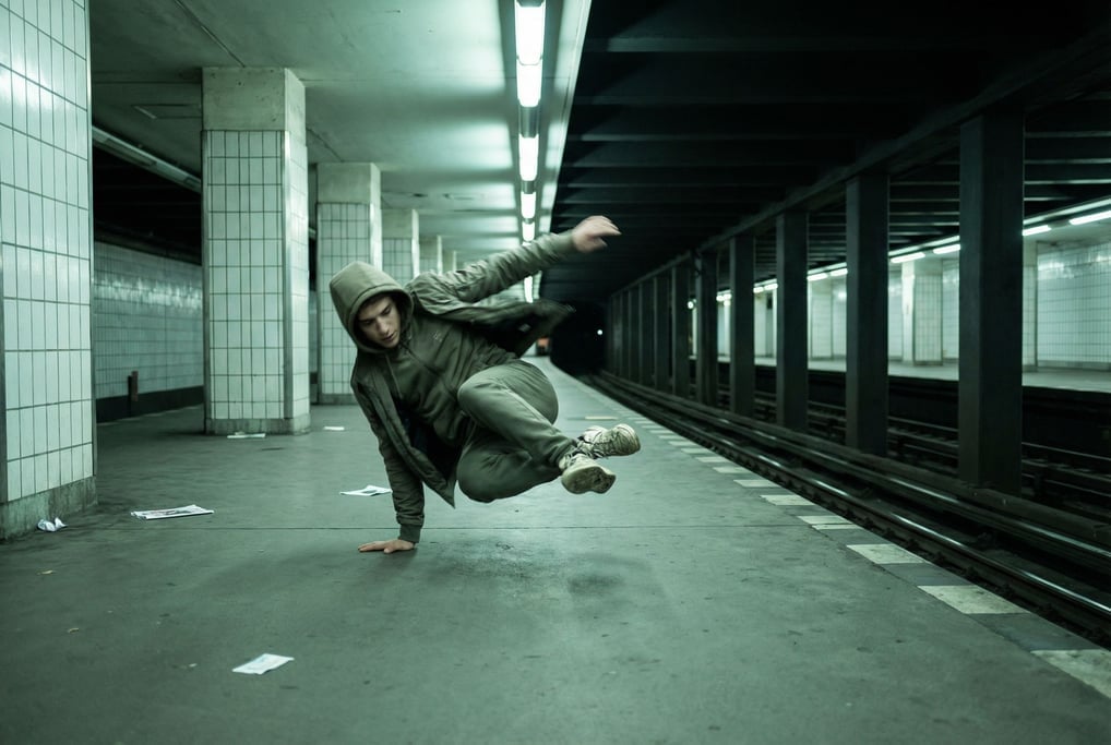 A man in his 20s breakdancing alone in an empty subway station at night