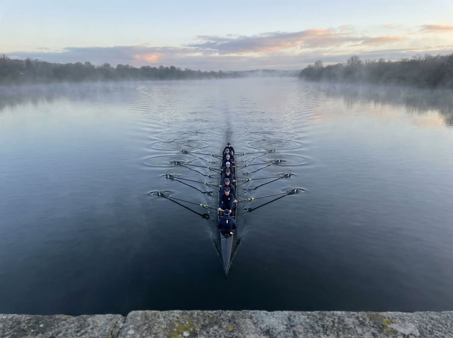 A dawn rowing crew on a river, eight rowers and a coxswain in perfect synchronization