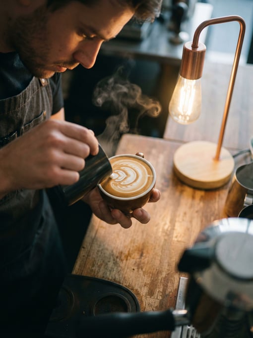 A barista pouring latte art, shot from above, steam and swirl patterns in the milk (07lhawdd)