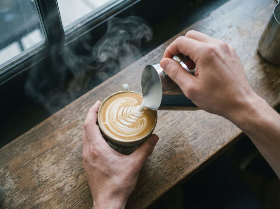 A barista pouring latte art, shot from above, steam and swirl patterns in the milk (n68xqq4z)