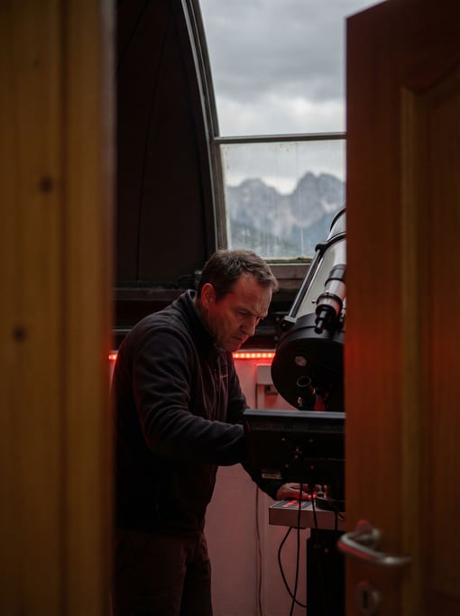 An astronomer at a telescope in a mountaintop observatory, red light preserving night vision (5n9ifcuo)