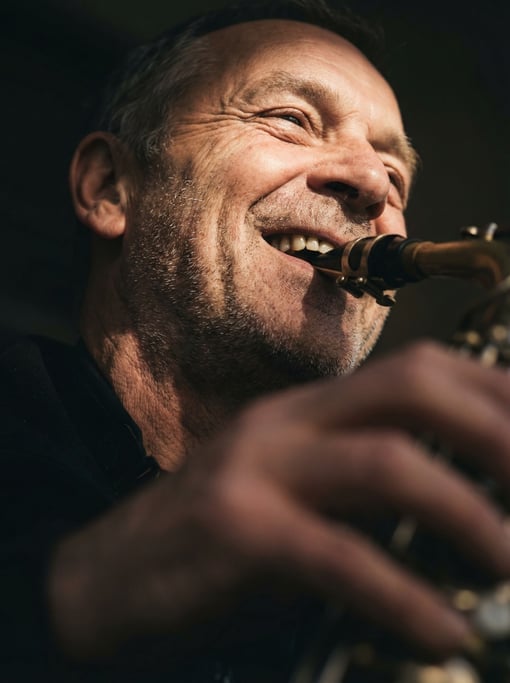 A street musician playing saxophone under a pool of streetlight, everything else in shadow (humbrgd)