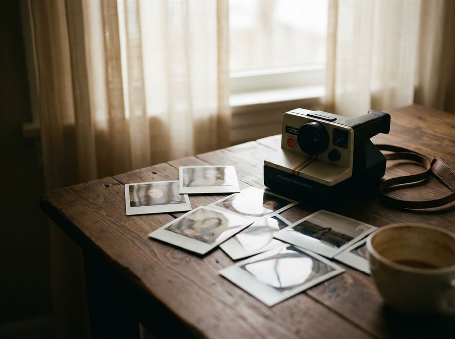 Polaroid photos scattered around an instant camera on a dark wood surface (nvyqlqj2)