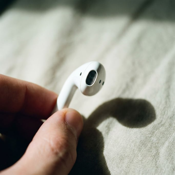 A hand holding a single AirPod between thumb and forefinger, macro on the mesh and seams (vw1axa8p)