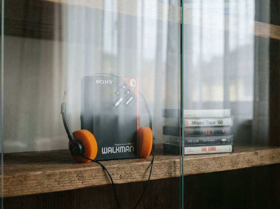 A vintage Walkman with foam headphones on a wooden shelf next to cassette tapes (dsav2jhi)