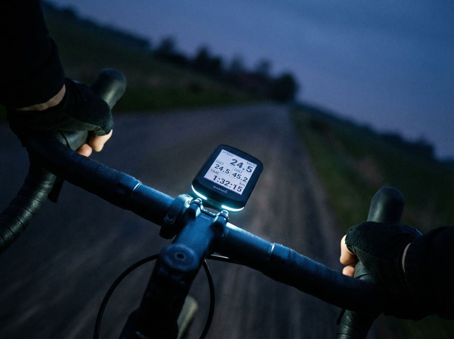 A bicycle computer mounted on handlebars, displaying stats, road blurred below (78aeofuc)