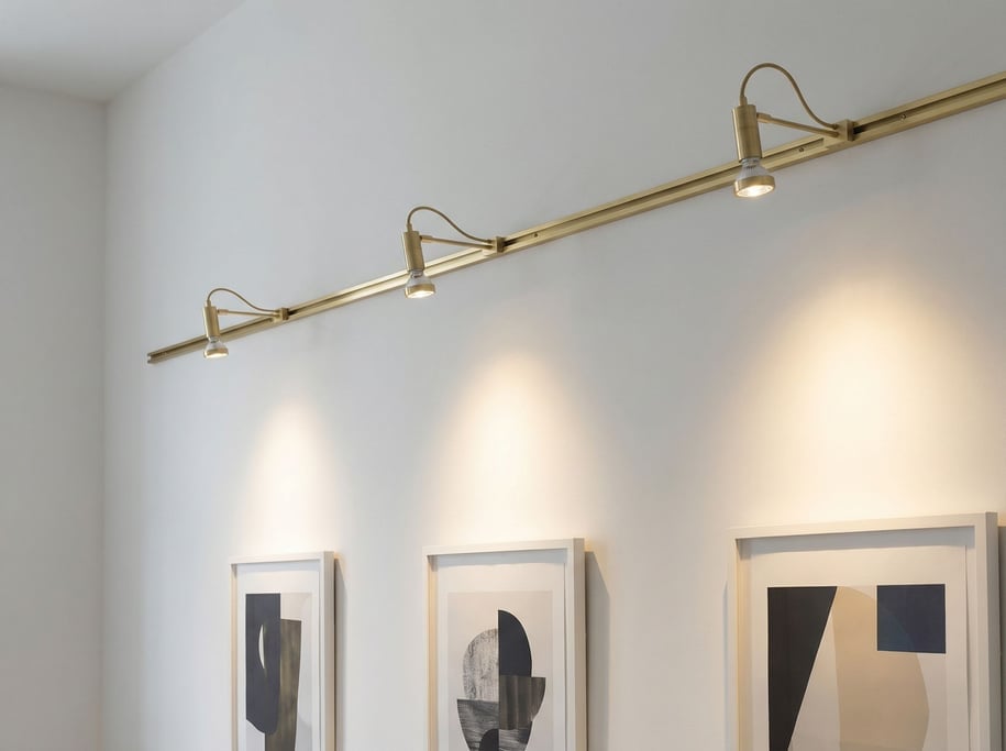Three small adjustable LED spotlights clip at intervals along a thin brushed brass picture rail track