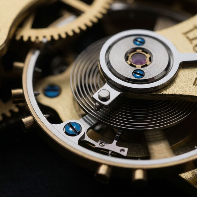 The balance wheel of a watch movement spins at macro magnification — hairspring coiled in a perfect Archimedes spiral