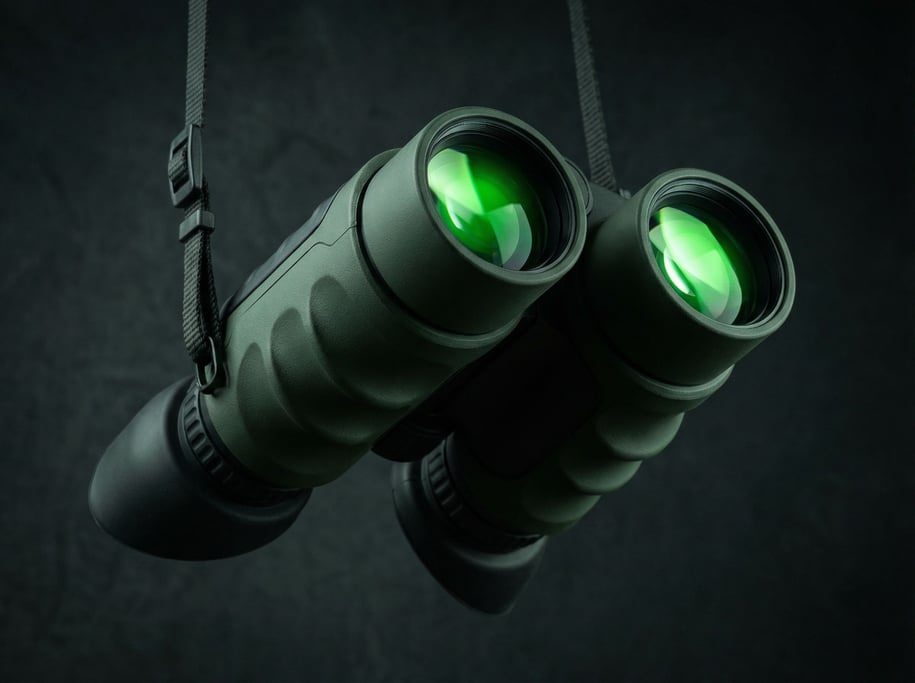A concept night vision binocular hangs from a neck strap against dark background — dual large objective lenses coated green
