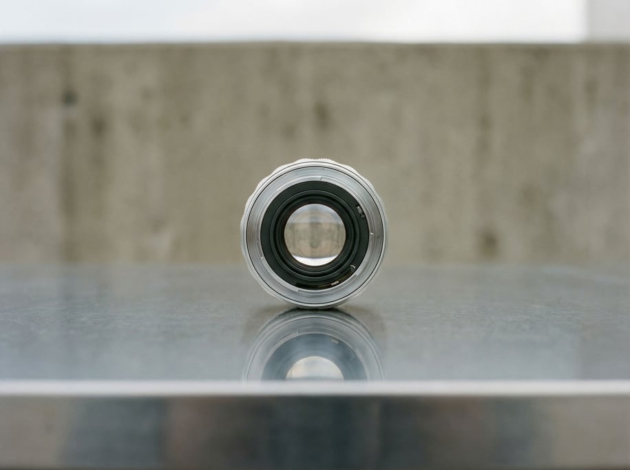 A camera lens standing upright on a reflective surface, internal elements visible through glass (e4ukgmub)