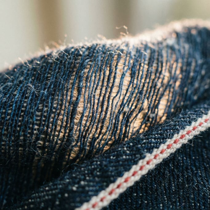 Extreme close-up of Raw denim fabric macro, indigo threads against white weft, visible selvedge edge
