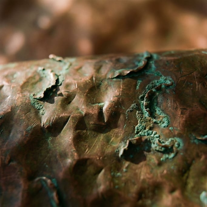 Detail photograph of Hammered copper sheet with dents and oxidation turning green at the edges