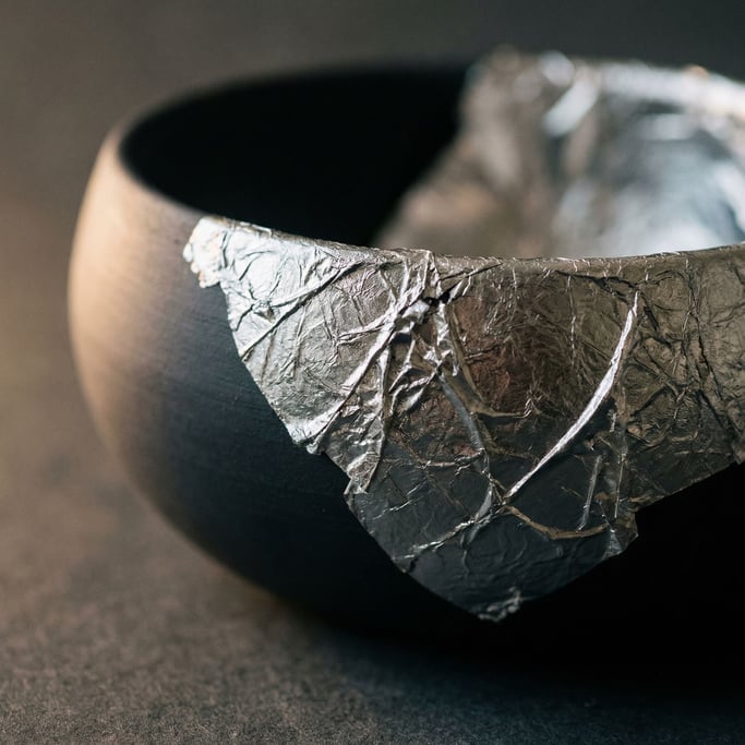 Crumpled silver leaf on a matte dark surface, fragile and luminous