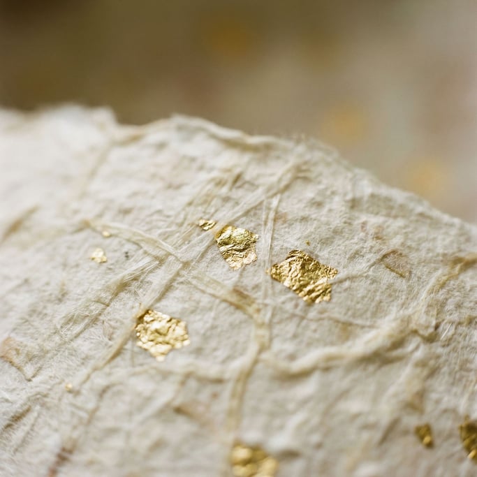 Extreme close-up of Japanese washi paper with embedded gold leaf flecks, translucent fibers