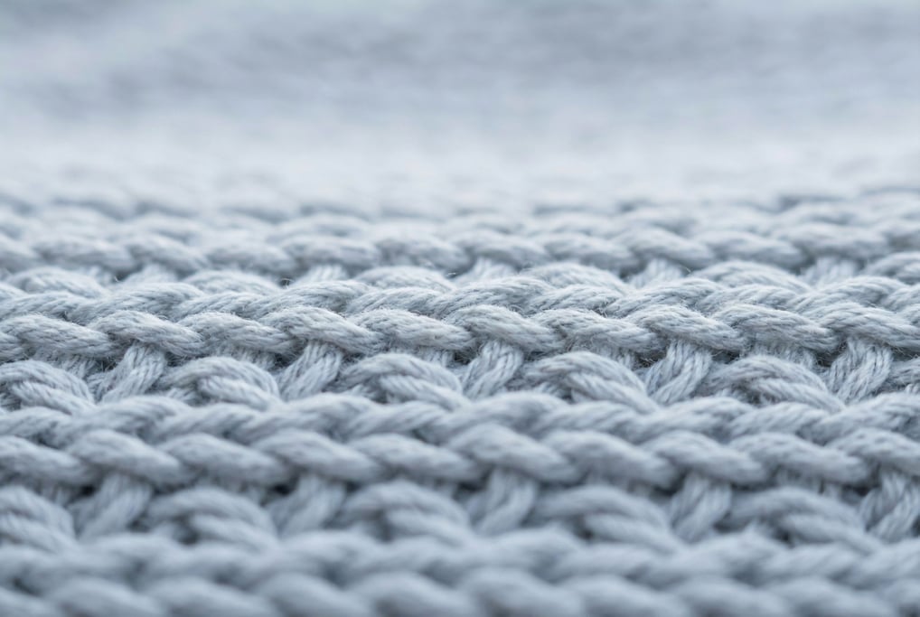 Pale grey jersey knit at extreme magnification revealing the V-shaped knit stitch pattern in perfect repeating rows