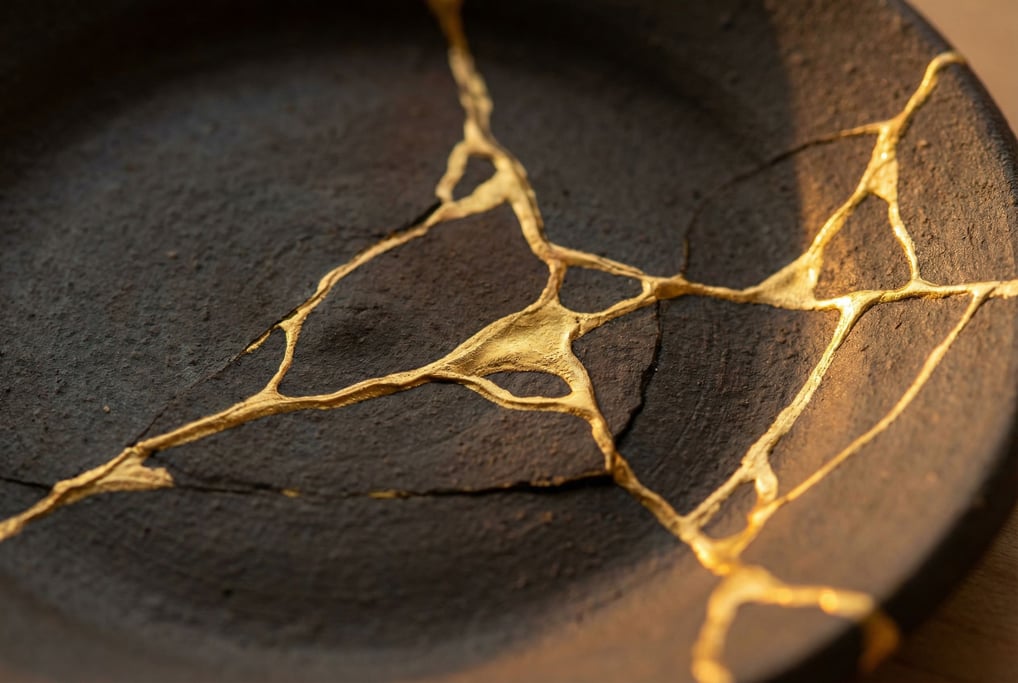Kintsugi repair lines in gold across dark stoneware filling the frame