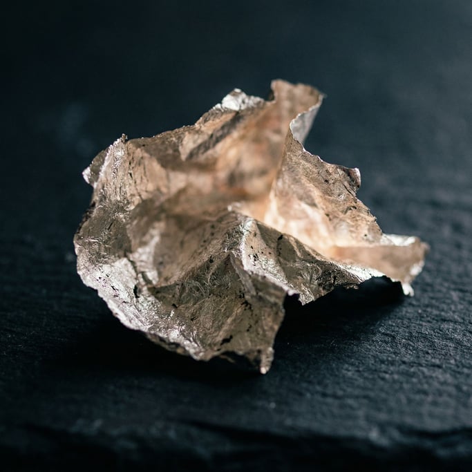 Extreme close-up of Crumpled silver leaf on a matte dark surface, fragile and luminous (8b2uu5zq)