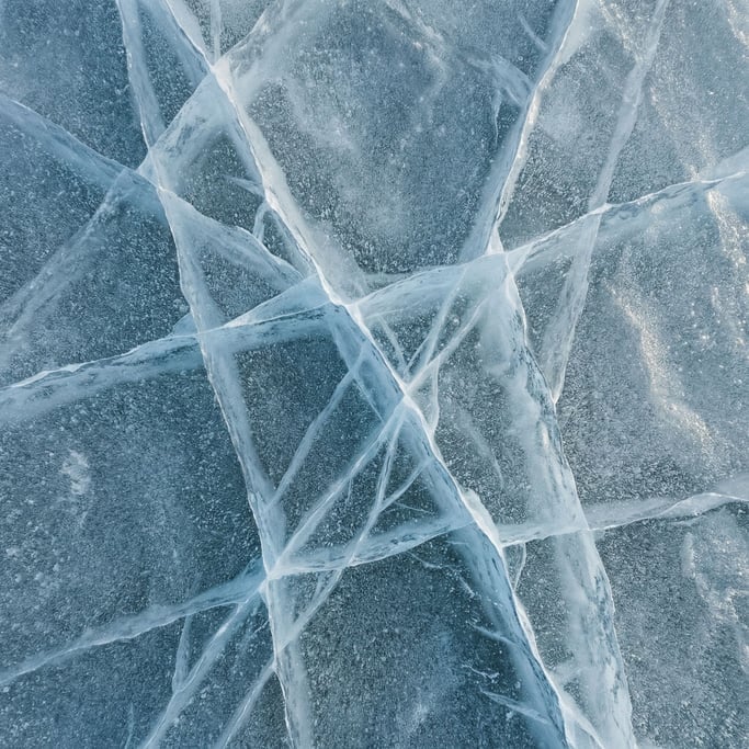 Extreme close-up of Ice sheet cracking, blue-white fracture lines across a frozen surface (ch43nyv4)