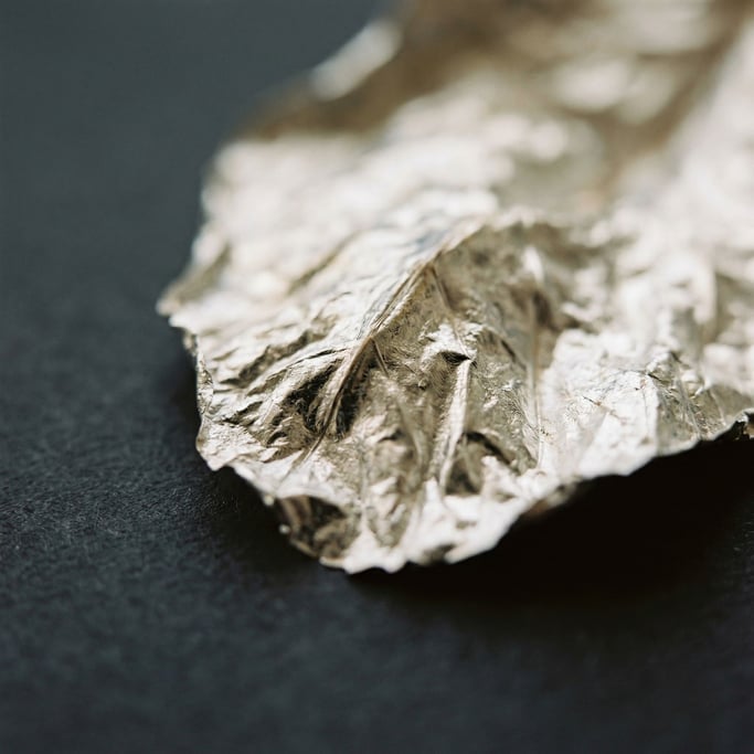 Extreme close-up of Crumpled silver leaf on a matte dark surface, fragile and luminous (pkcajta)