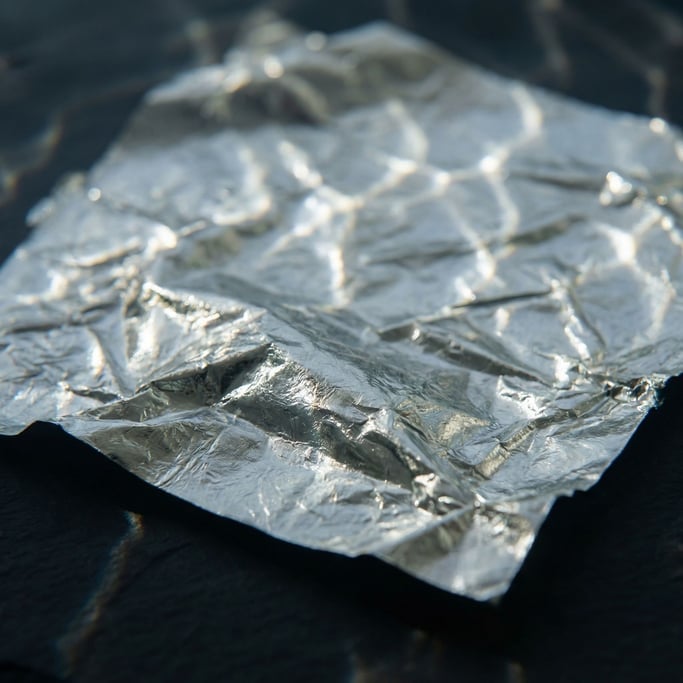Detail photograph of Crumpled silver leaf on a matte dark surface, fragile and luminous (er44iq9)
