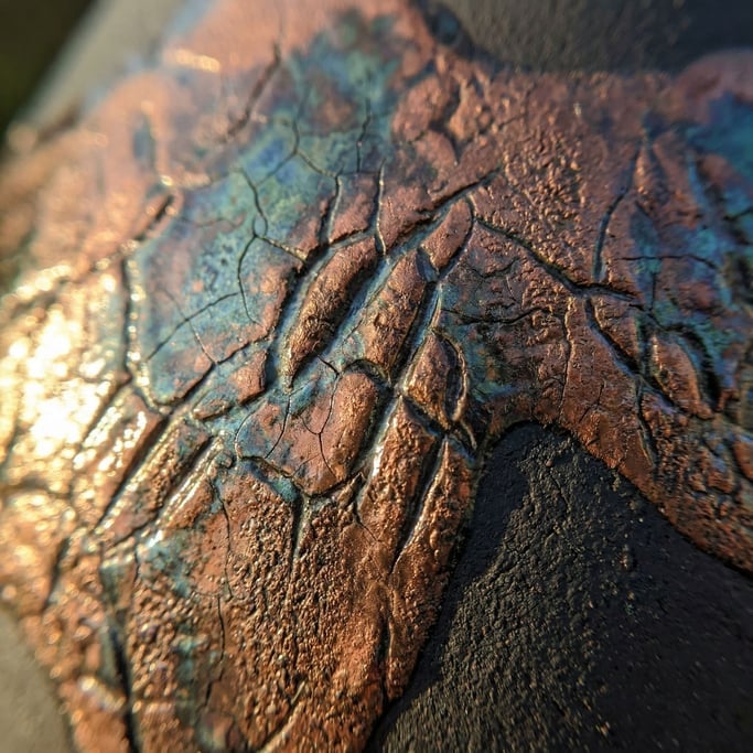 Extreme close-up of Ceramic raku glaze, metallic copper reduction over black clay body