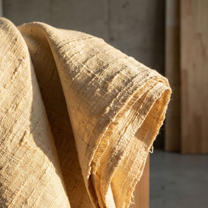 Raw silk fabric draped and catching side light, subtle sheen and woven texture visible