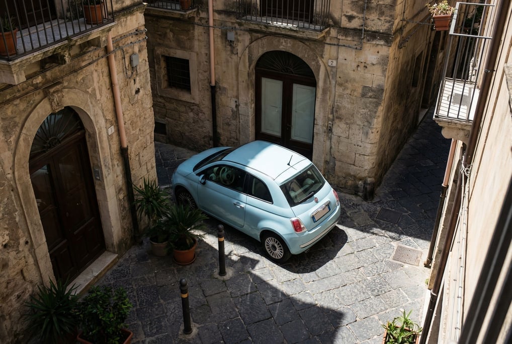 Compact city car in pastel blue squeezed into a tight European parking space between stone buildings