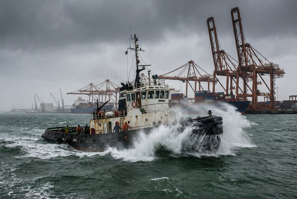 Tugboat pushing through choppy harbor water, spray crashing over the bow