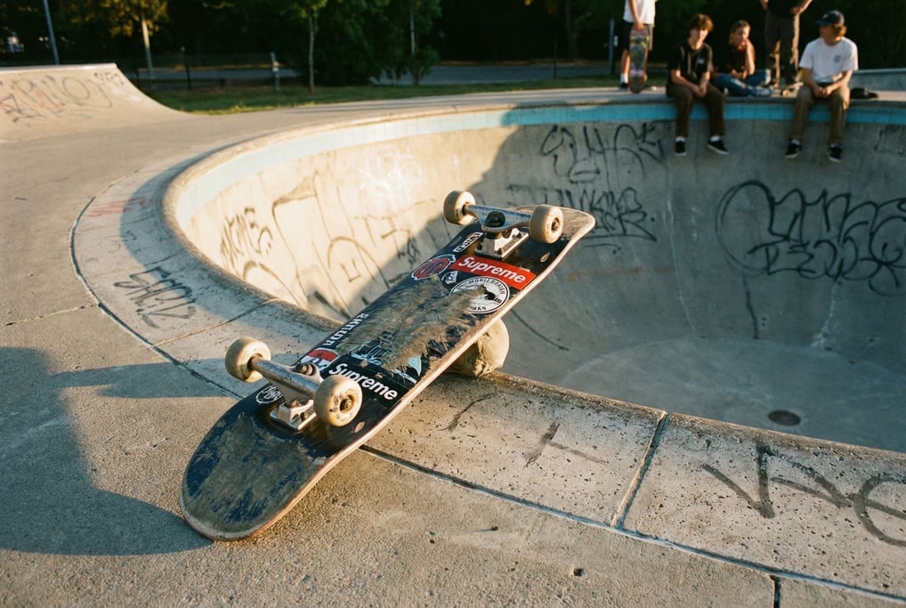 Skateboard resting on its side at the lip of an empty concrete pool at a skatepark