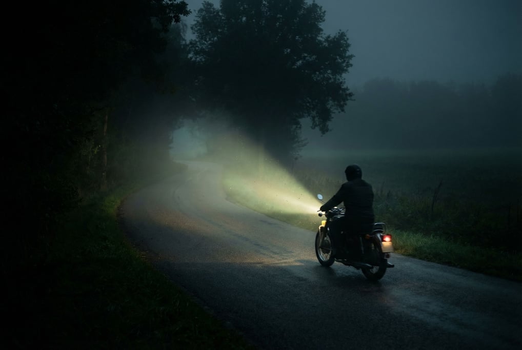 Motorcycle headlight beam cutting through fog on a rural road at night