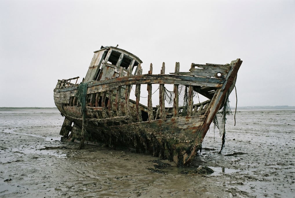 Derelict fishing boat beached on a mudflat at low tide, hull listing to one side