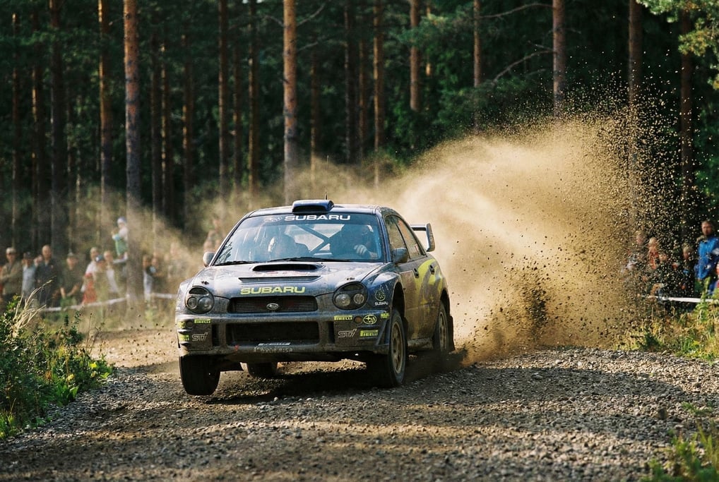 Rally car kicking up a plume of gravel on a forest stage, dirt spraying in an arc