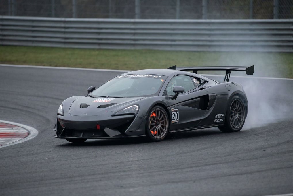 Track-day sports car braking hard into a corner, front wheels turned, brake disc glowing faintly