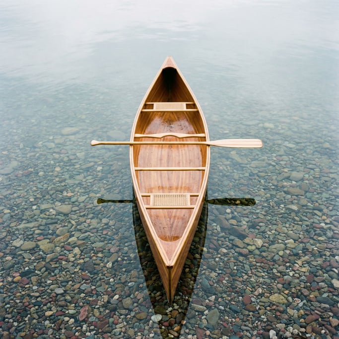 Overhead view of a canoe on a crystal-clear lake, the paddle resting across the gunwales