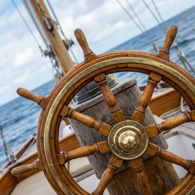 Ship's wheel in varnished teak and brass, mounted on a classic sailing yacht