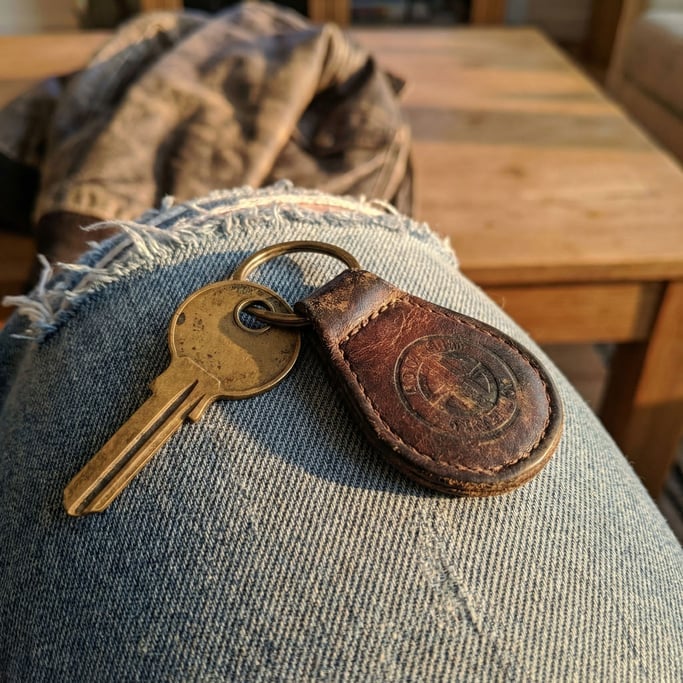 Classic car key on a leather fob resting on a worn denim surface, brass key shaft and round head