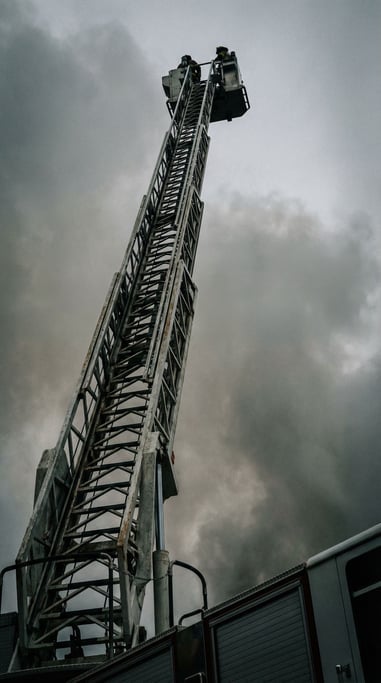 Narrow shot of a fire truck ladder extended fully upward against a smoky grey sky