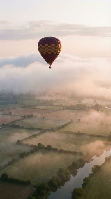 Hot air balloon in maroon and gold ascending through morning mist
