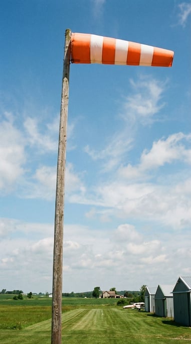 Windsock on a tall pole at a rural airstrip, fully extended in a stiff breeze