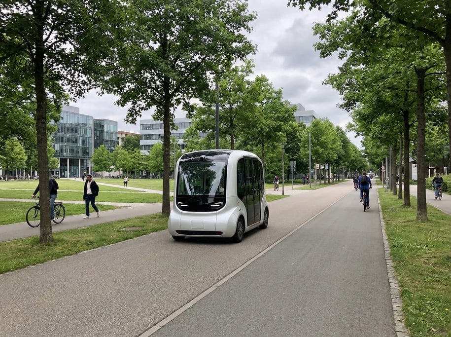 Autonomous shuttle in smooth white bodywork on a dedicated lane through a park-like campus