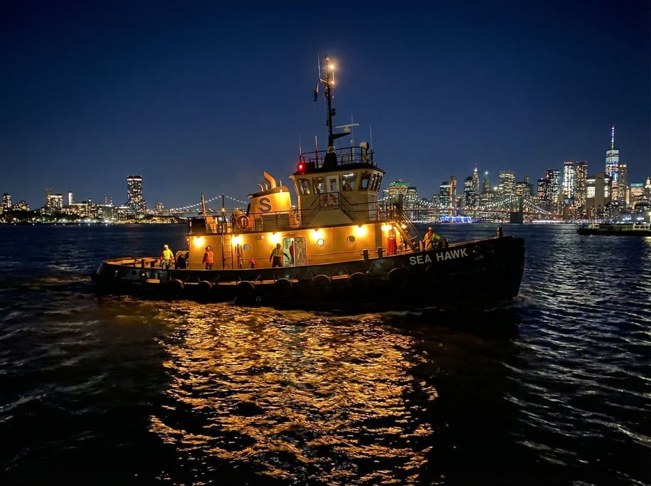 Tugboat in a harbor at night, working lights illuminating the deck