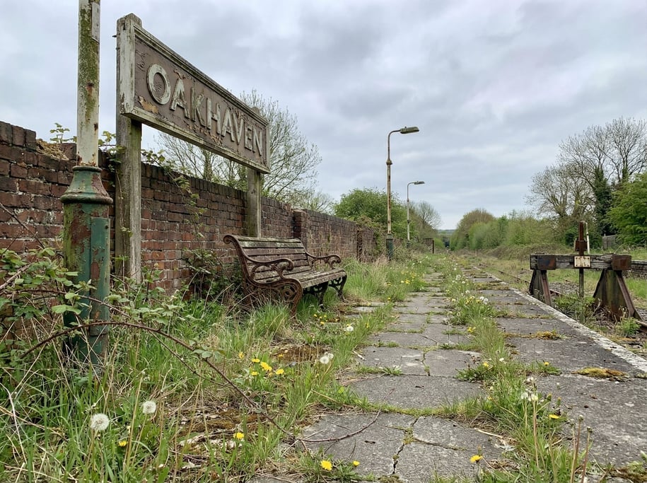 Overgrown railway platform with weeds pushing through the concrete, a rusted bench