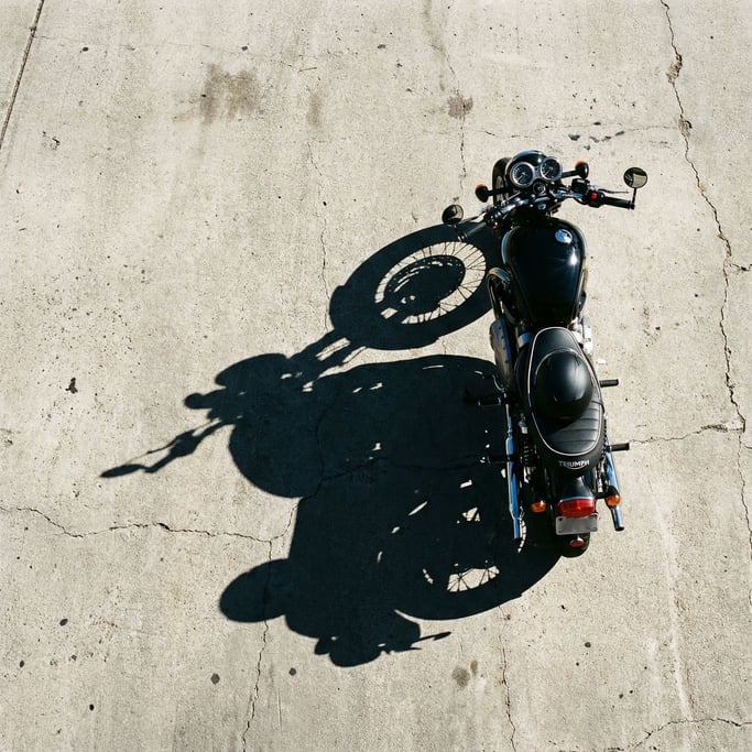 Overhead view of a motorcycle and its shadow on sunlit concrete