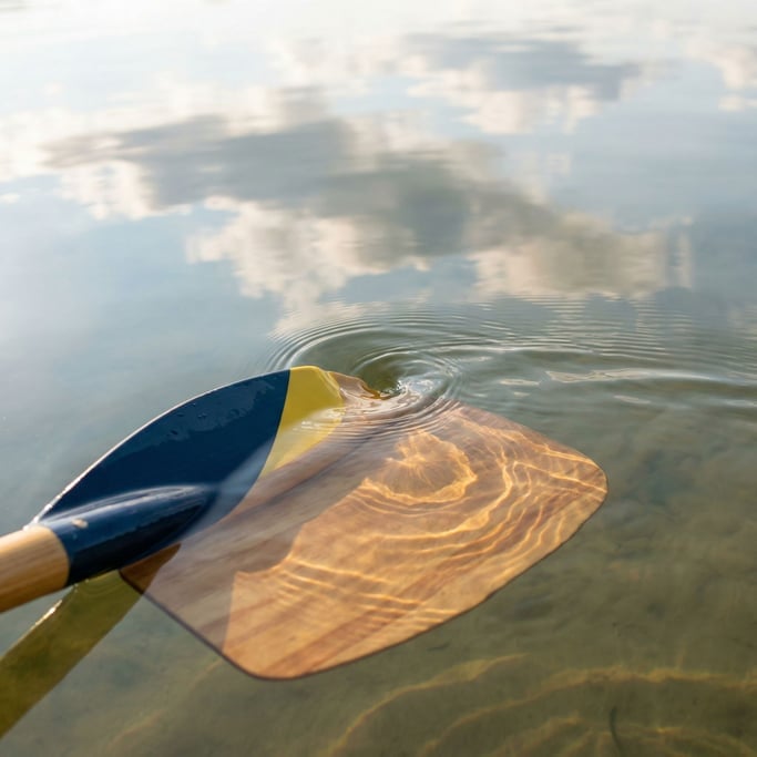 Kayak paddle blade half-submerged in glassy lake water, the paddle creating a small vortex