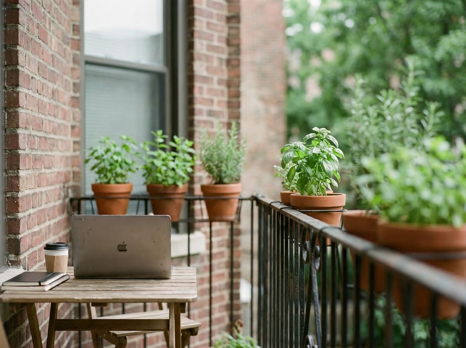 A fire escape workspace in summer, laptop on a small folding table, brick wall behind (4yhodrb)