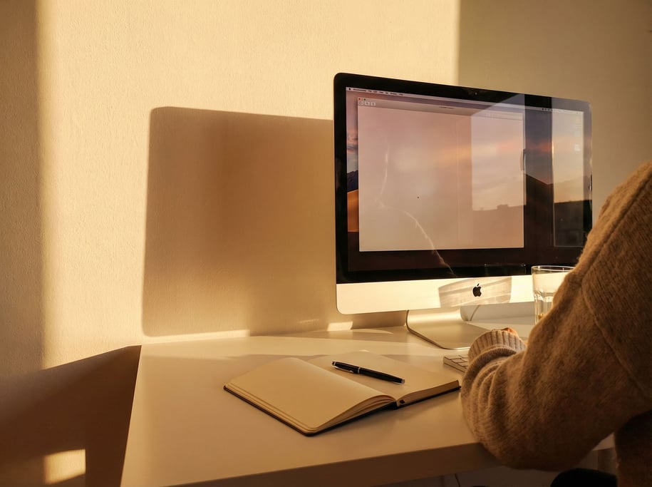 A clean white desk with an iMac, single notebook, and a pen, everything aligned and minimal (qhl8er5f)