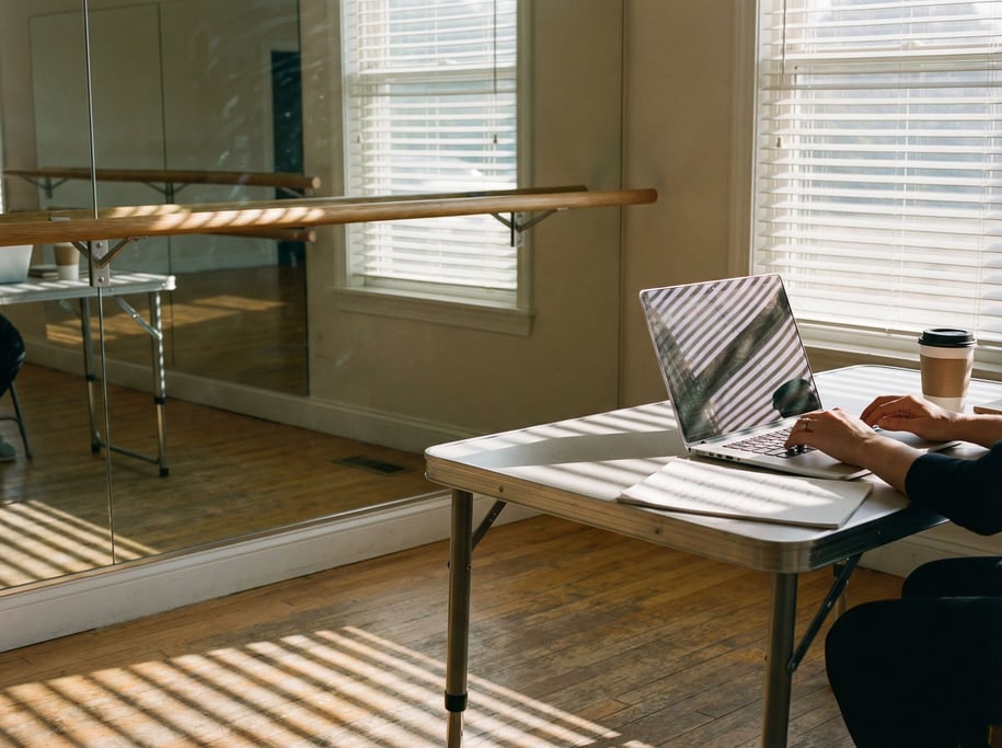 A ballet studio office corner, laptop on a folding table against a mirrored wall