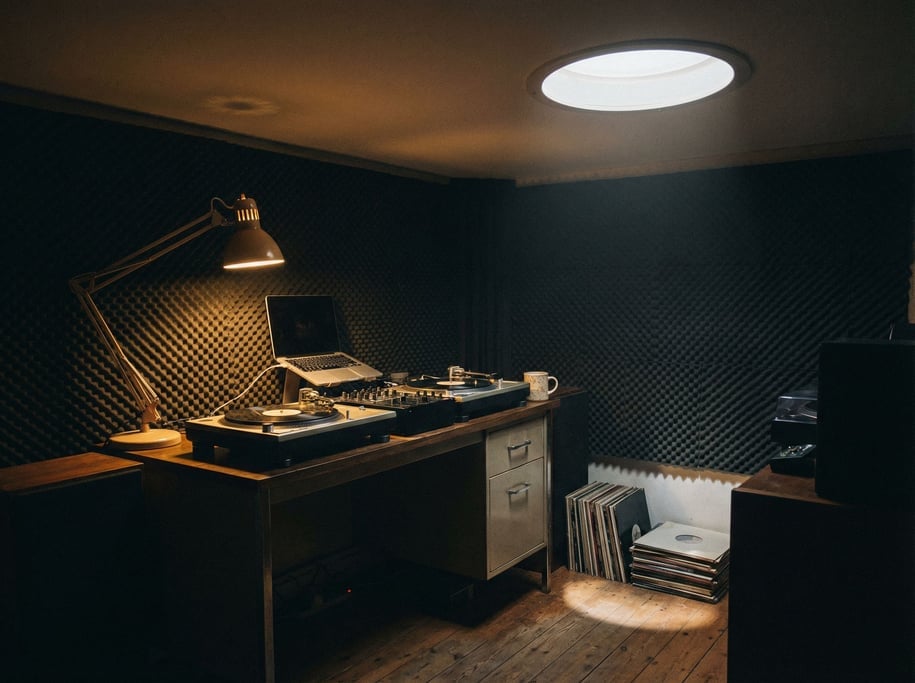 A vinyl DJ's home studio, laptop next to turntables and a mixer, acoustic foam panels on the wall (1dy0e45j)